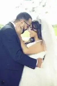 square_4_media Bride and groom in wedding attire embrace closely outdoors, smiling as they touch foreheads. media_agency