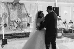 square_4_media A bride and groom share a first dance at their wedding reception, with floral decorations and guests visible in the background. media_agency