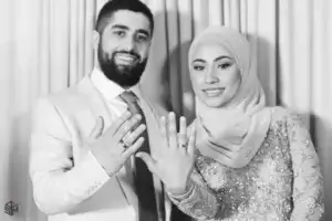 square_4_media A man and woman smile at the camera, each holding up a hand to display rings on their fingers. The woman wears a hijab and an embroidered outfit. media_agency