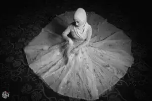 square_4_media A woman in a hijab and embellished dress sits on the floor with her gown fanned out in a circle around her, photographed from above in black and white. media_agency