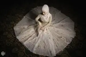 square_4_media A woman in a pale, embellished gown and hijab sits on a dark patterned floor with her dress fanned out around her in a circular shape. media_agency