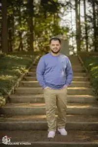 square_4_media A man in a blue sweatshirt and khaki pants stands on a brick path in front of outdoor steps surrounded by trees and greenery. media_agency