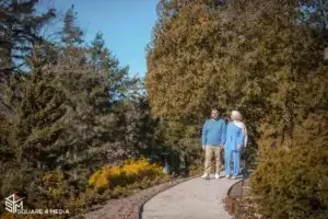 square_4_media A man and woman walk together on a curved path surrounded by trees and shrubs on a sunny day. media_agency