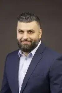 square_4_media Man with dark hair and beard wearing a navy blue suit jacket and light-colored shirt, posing for a professional portrait against a plain dark background. media_agency