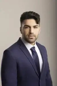 square_4_media A man in a navy blue suit, white shirt, and navy tie poses for a formal studio portrait against a plain light background. media_agency