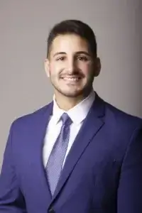 square_4_media A man wearing a blue suit, white dress shirt, and patterned tie smiles at the camera against a plain, light-colored background. media_agency