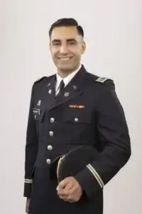 square_4_media A man in a formal military uniform stands smiling, holding a black service cap in his left hand against a plain light background. media_agency