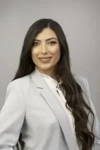 square_4_media A woman with long dark hair wearing a light-colored blazer and white blouse poses in front of a plain background, smiling at the camera. media_agency