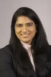 square_4_media A woman with long dark hair and medium skin tone, wearing a black blazer and light-colored blouse, smiles at the camera against a plain background. media_agency