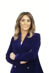 square_4_media Woman with wavy brown hair in a blue blazer smiles with arms crossed against a plain white background. media_agency