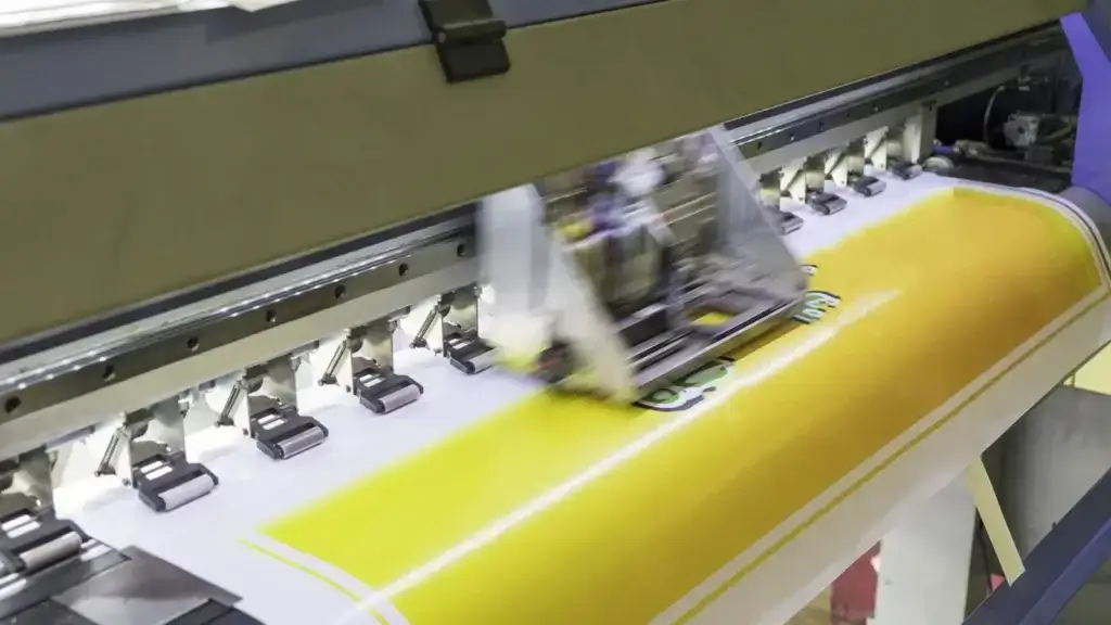 square_4_media A large commercial printer prints a yellow and white banner with green text and graphics on a continuous sheet. media_agency square_4_media A large commercial printer prints a yellow and white banner with green text and graphics on a continuous sheet. media_agency