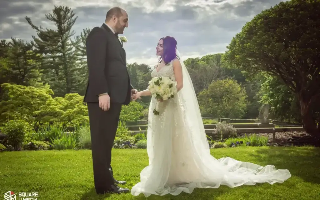 square_4_media A bride and groom stand outdoors on grass, holding hands and smiling at each other, with greenery and trees in the background. media_agency square_4_media A bride and groom stand outdoors on grass, holding hands and smiling at each other, with greenery and trees in the background. media_agency
